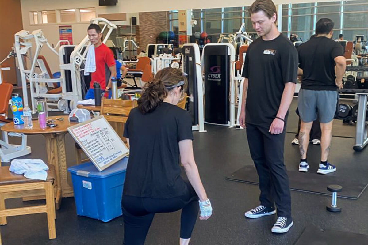A kinesiology student guides an employee through an exercise routine in the gym.