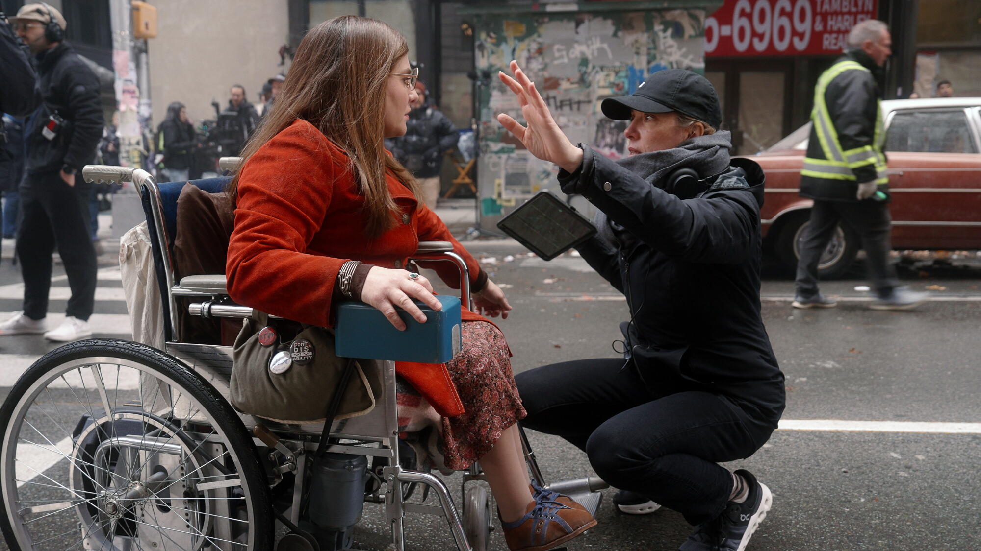 A woman using a wheelchair gets a note from a crouching director.
