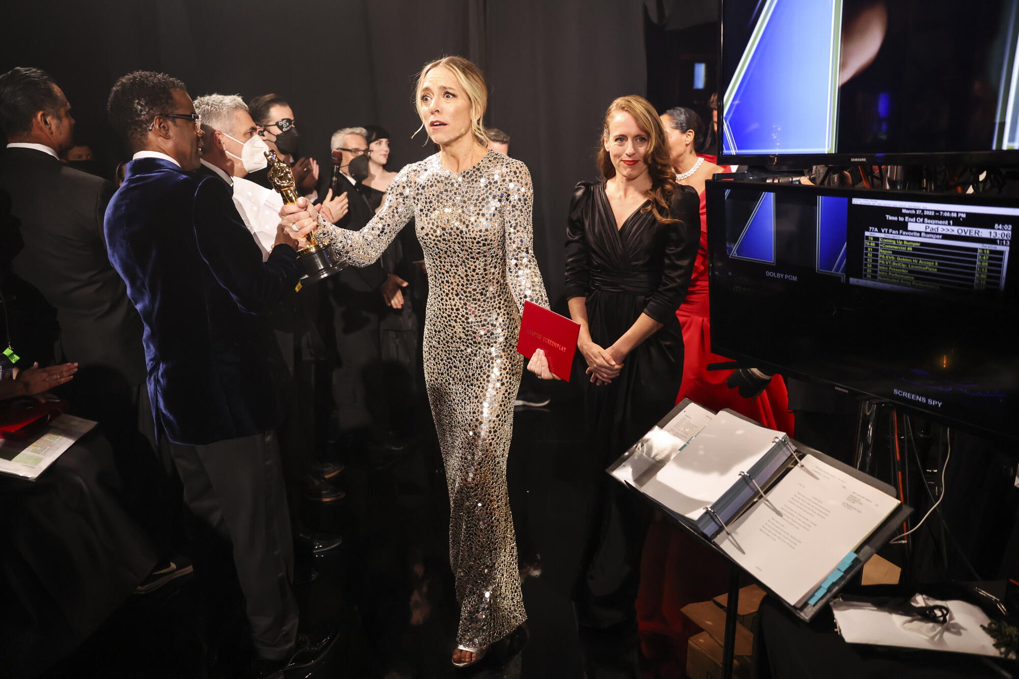 A woman in a gold dress holds an Oscar and a red envelope.