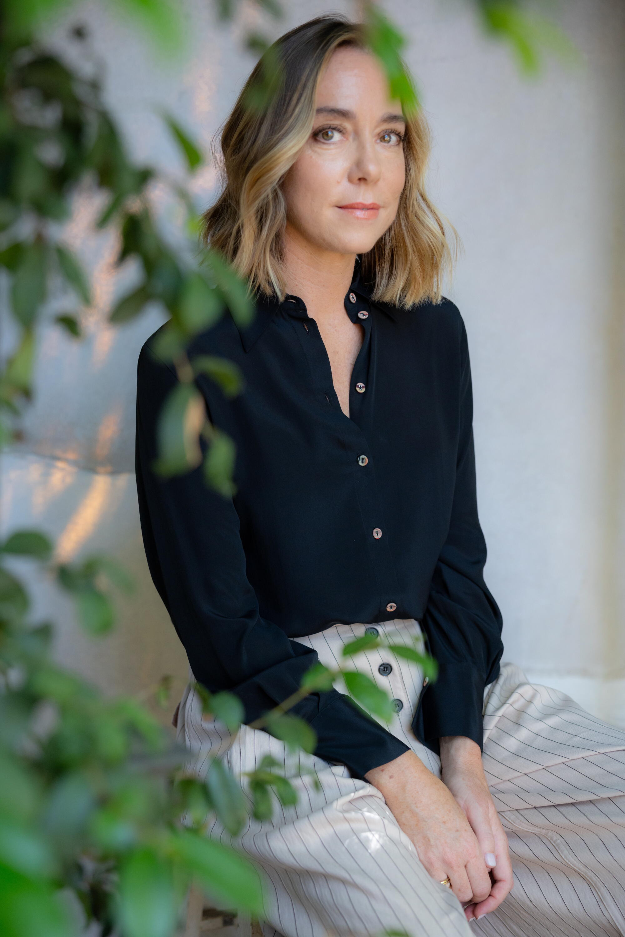 A woman sits behind a leafy tree.