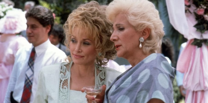 Two women with light skin tone stand next to each other in formal clothing
