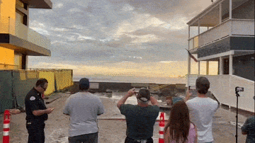 Massive waves crash along the Long Beach boardwalk as onlookers take video
