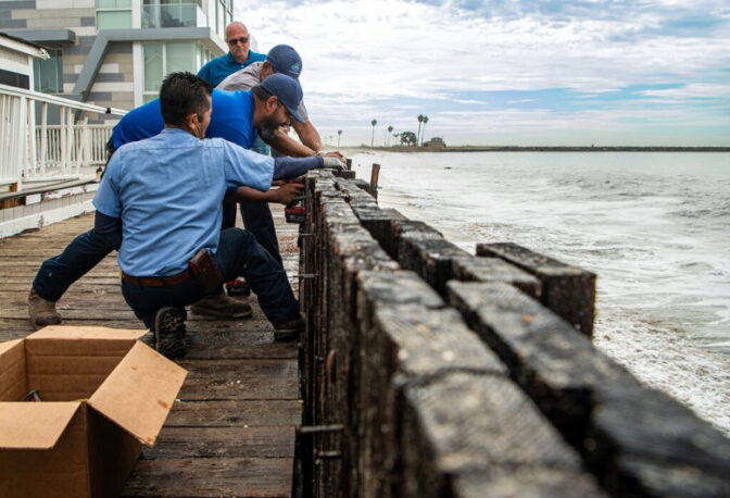 Workers work to bolt a seawall separate waves and homes next to a boardwalk.