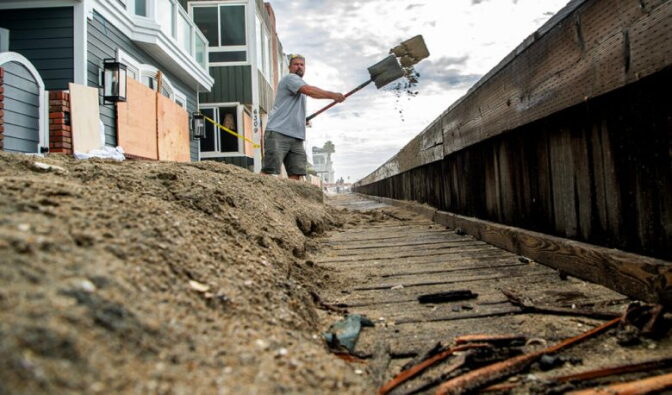 A low angle view of a man shoveling sand on a boardwalk over a sea barrier.