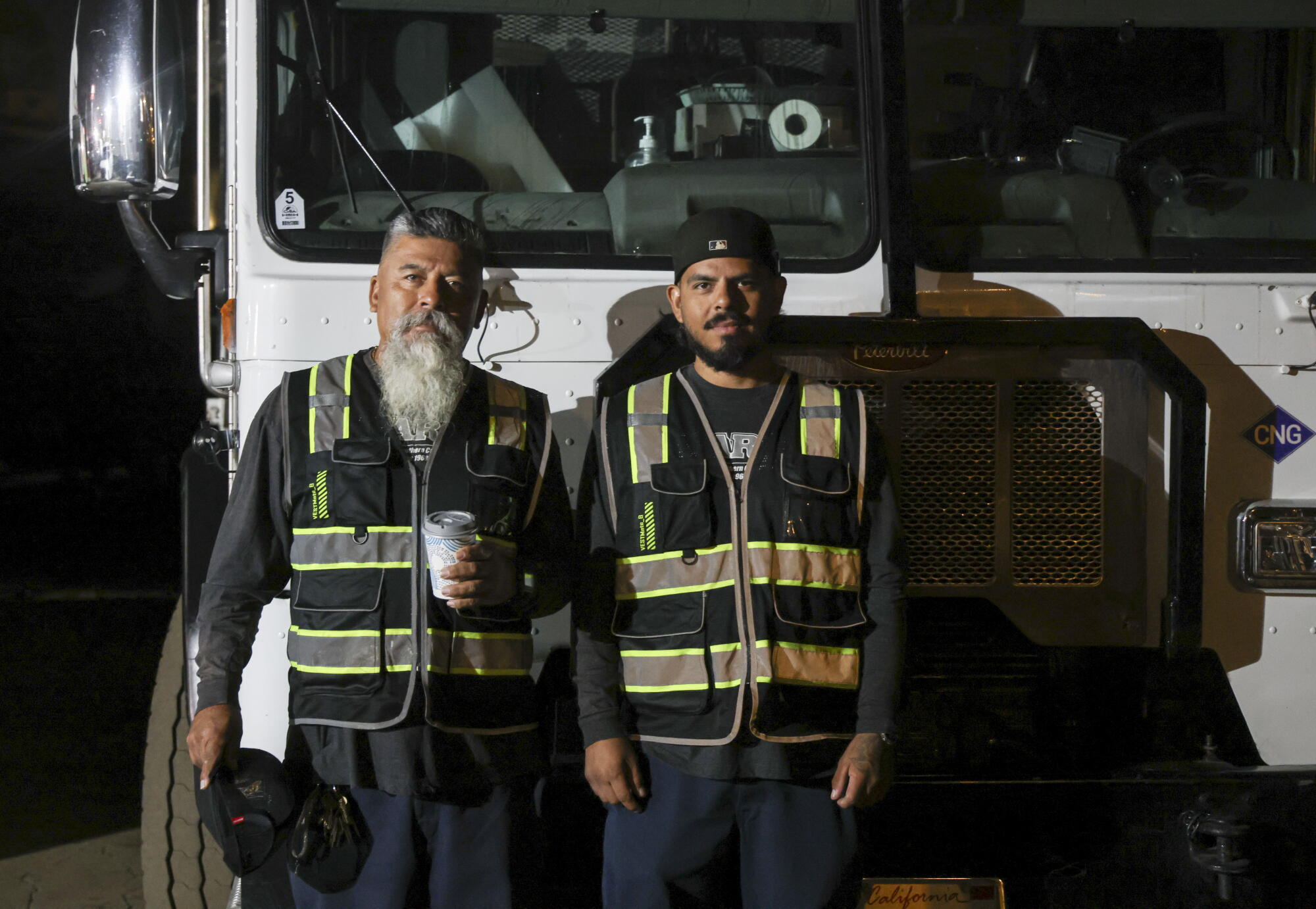 two workers pose in front of a sanitation truck