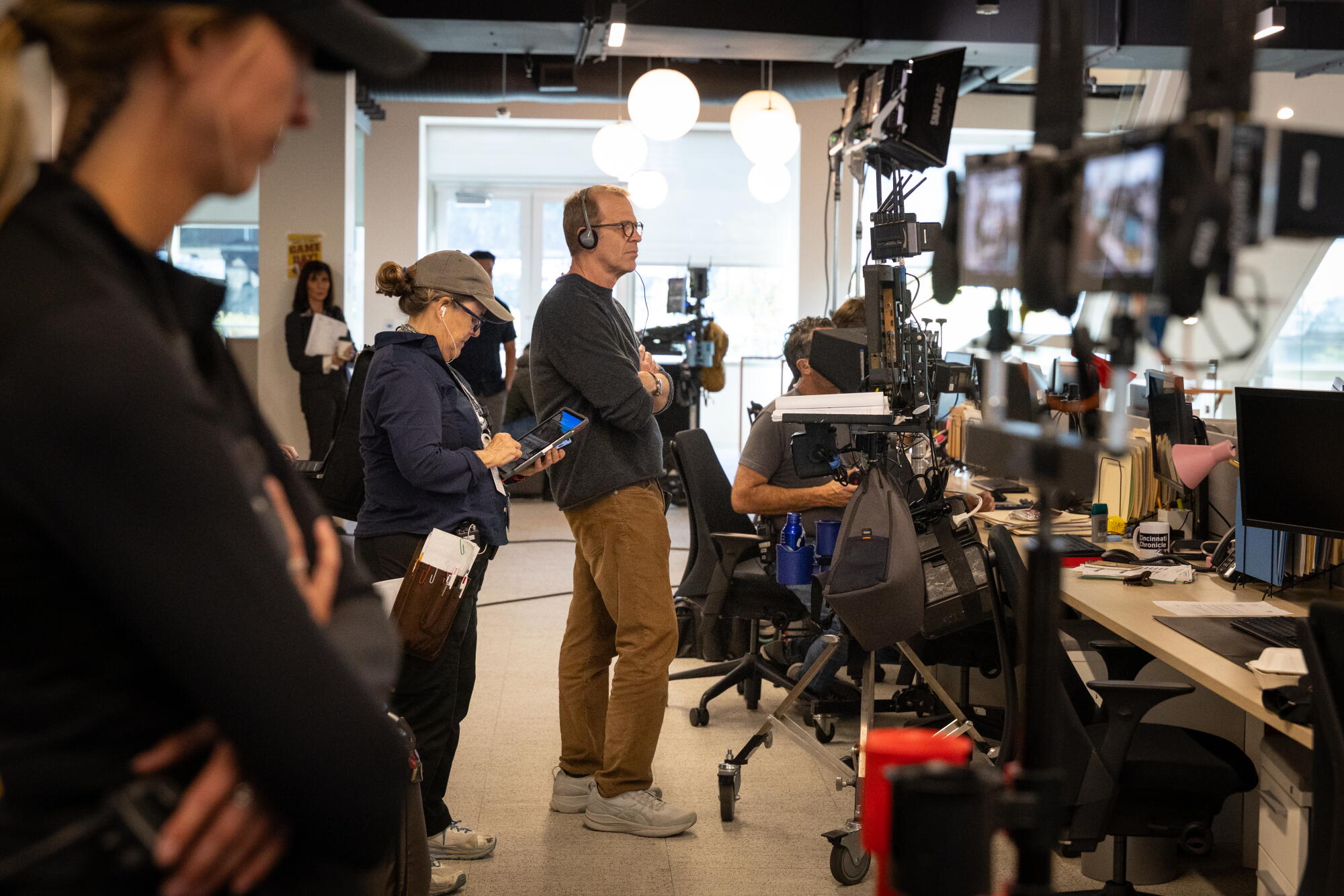 Crew members wearing headphones surrounded by film equipment and lights look at monitors.