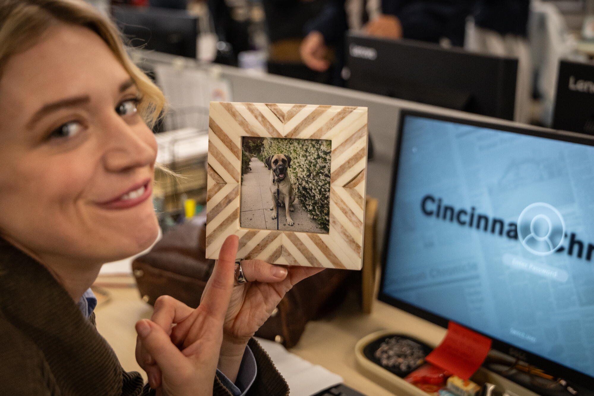 A blond woman points to a framed photo of a dog
