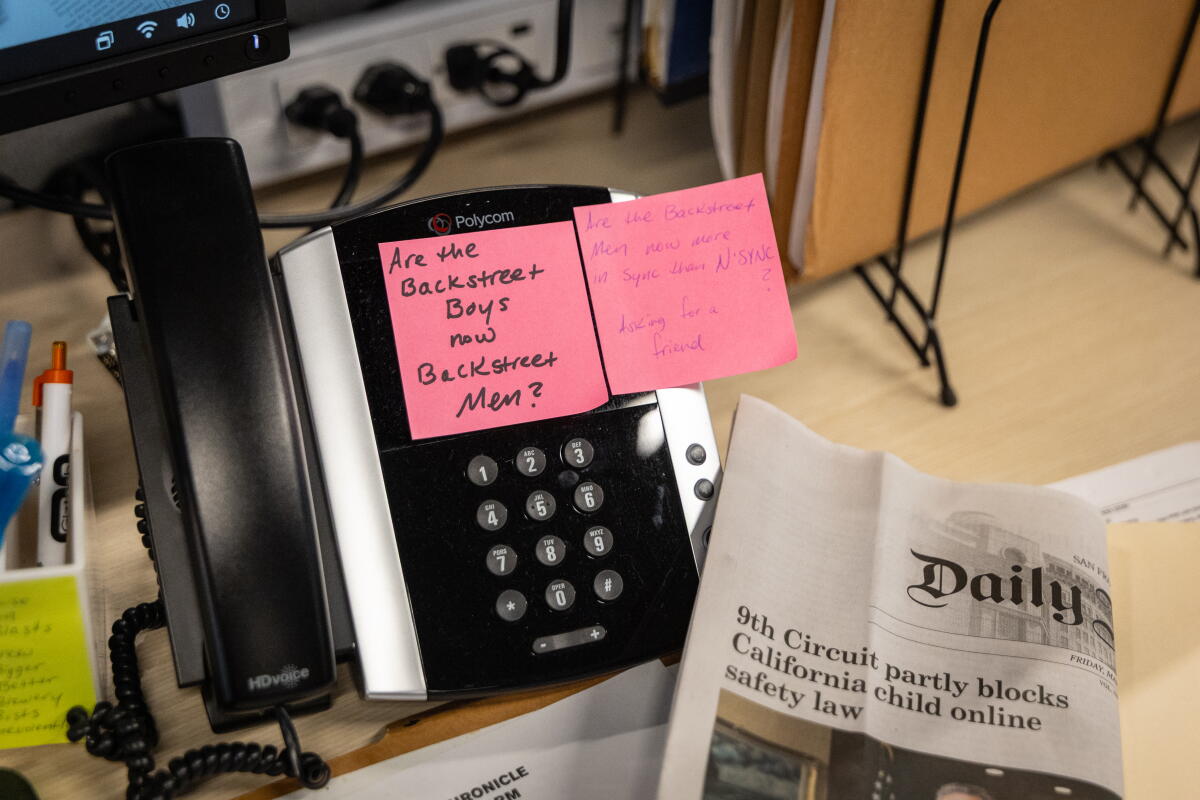 An image of a desk phone with pink sticky notes attached to it and a folded newspaper beside it.
