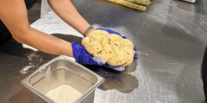 A woman's arms are seen with gloved hands holding a braided piece of dough ready to be baked.