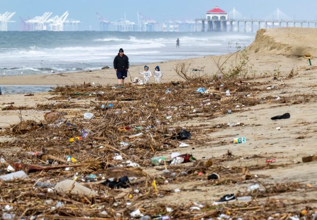 A man, dog and two kids walk near the pile of trash and debris on the beach that washed down the Santa Ana River in Huntington Beach on Monday, February 27, 2023 after the recent rain storms that hit Southern California. (Photo by Leonard Ortiz, Orange County Register/SCNG)