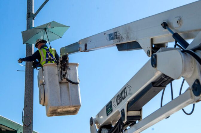 A close up and low angle view of a worker wearing a highlight yellow vest standing in a lift as he attaches a speed camera to a light pole.