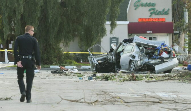 An officer walks towards a totaled car from a car accident in a parking lot.