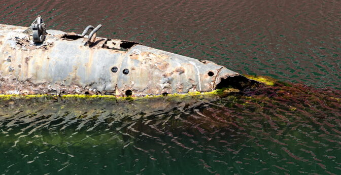 A close up of a rusted and deteriorating submarine in shallow water.