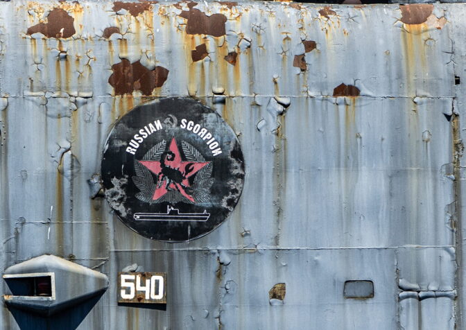 A close up of signage on a rusted submarine that reads "Russian Scorpion" with a scorpion design over a red star.