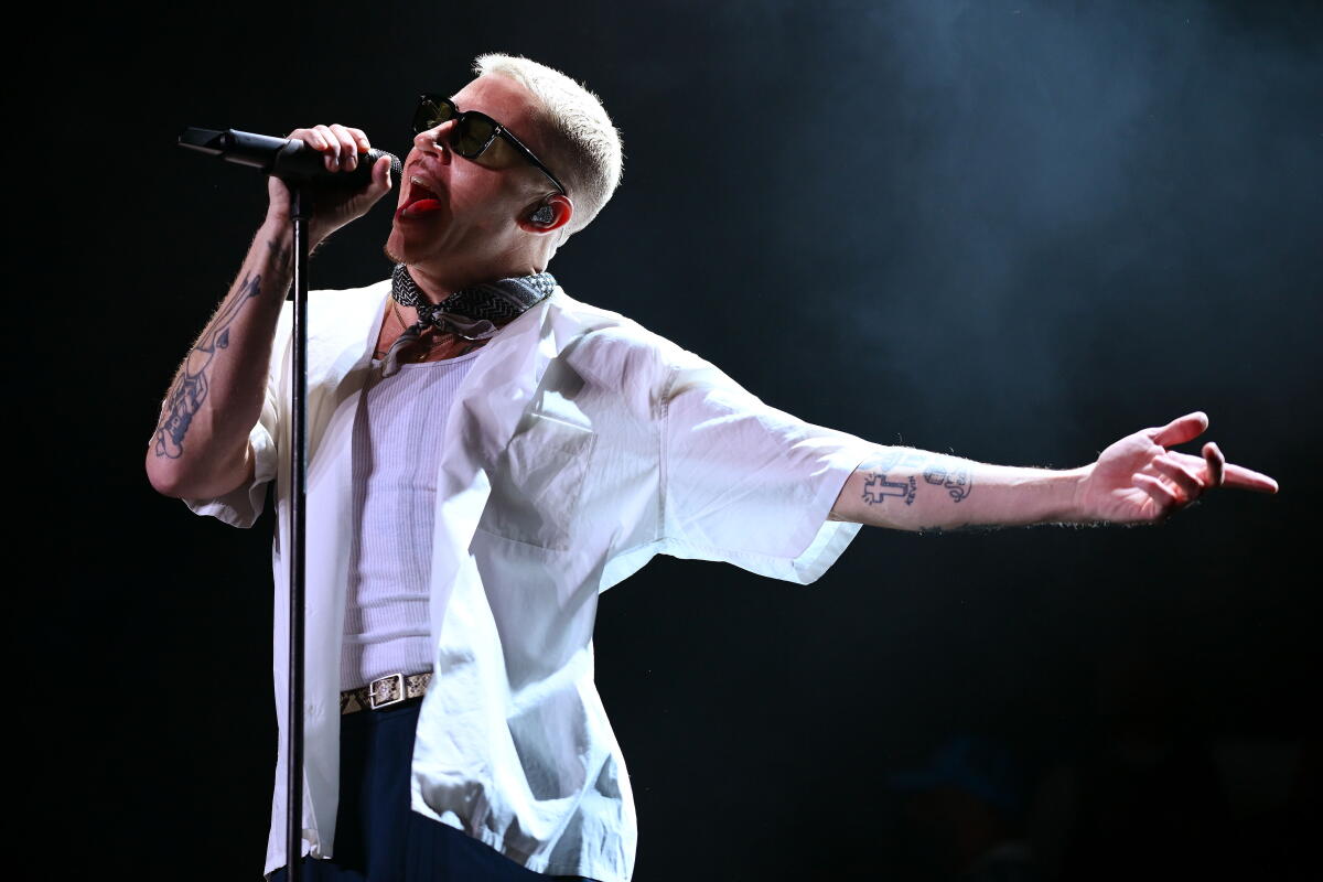 Macklemore performs holding a microphone on a stand with one arm held out