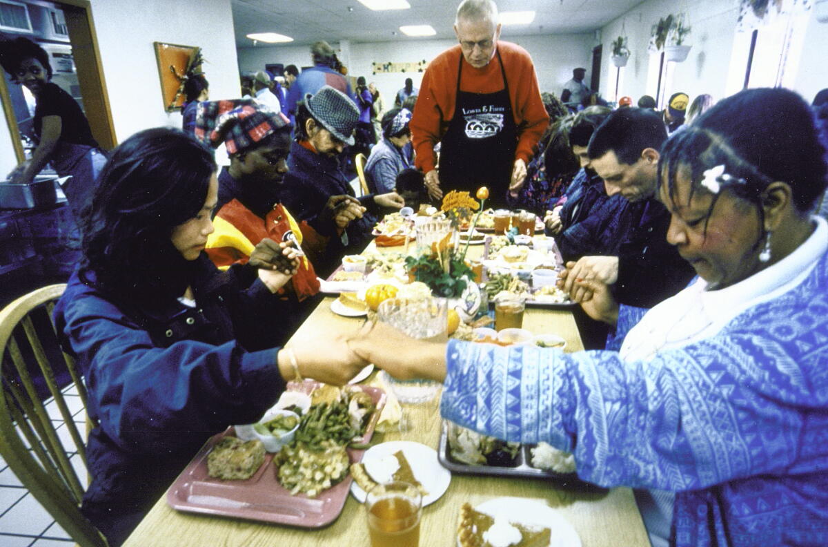 Leroy Chatfield, center back, saying a prayer over Thanksgiving dinner with some of his clients around, joining hands.