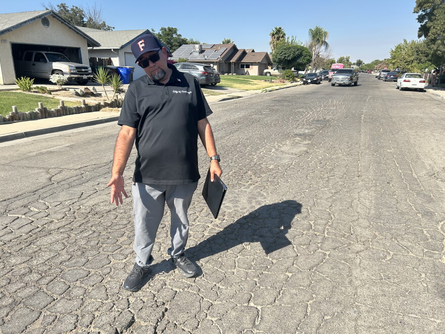 Firebaugh Mayor Freddy Valdez shrugs as he gestures toward the broken, cracked pavement on Yip Street in a residential part of town on Aug. 26, 2026.
