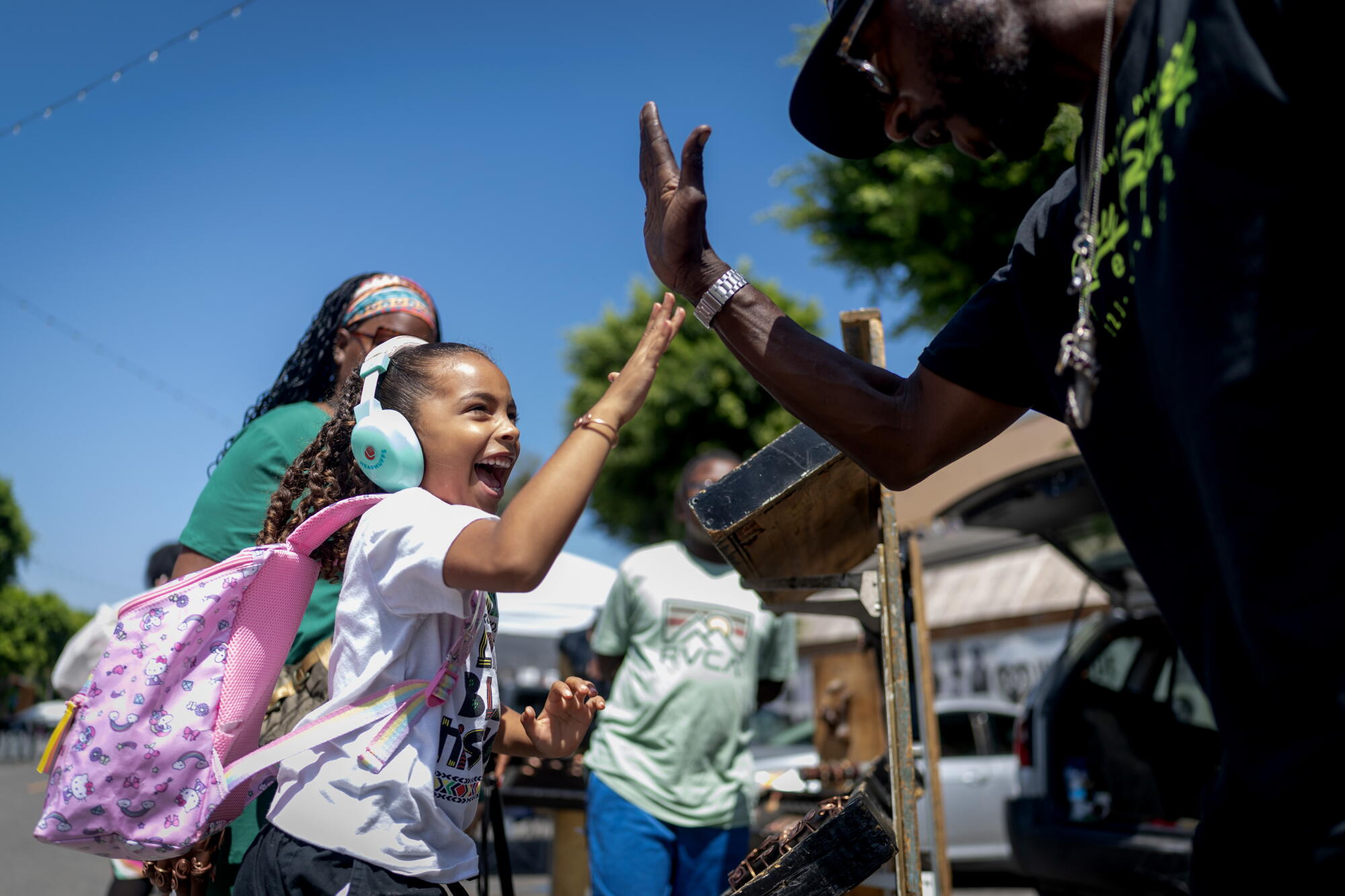 A young girl high-fives a jewelry maker named Ishmael during a weekly market in the Leimert Park.