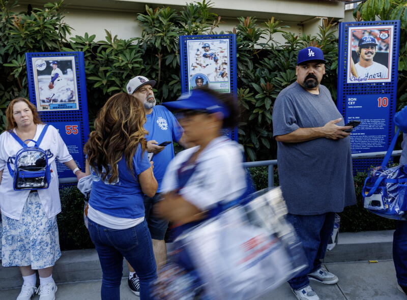 Dodgers fans walk past vibrant plants behind photos of former Dodgers.