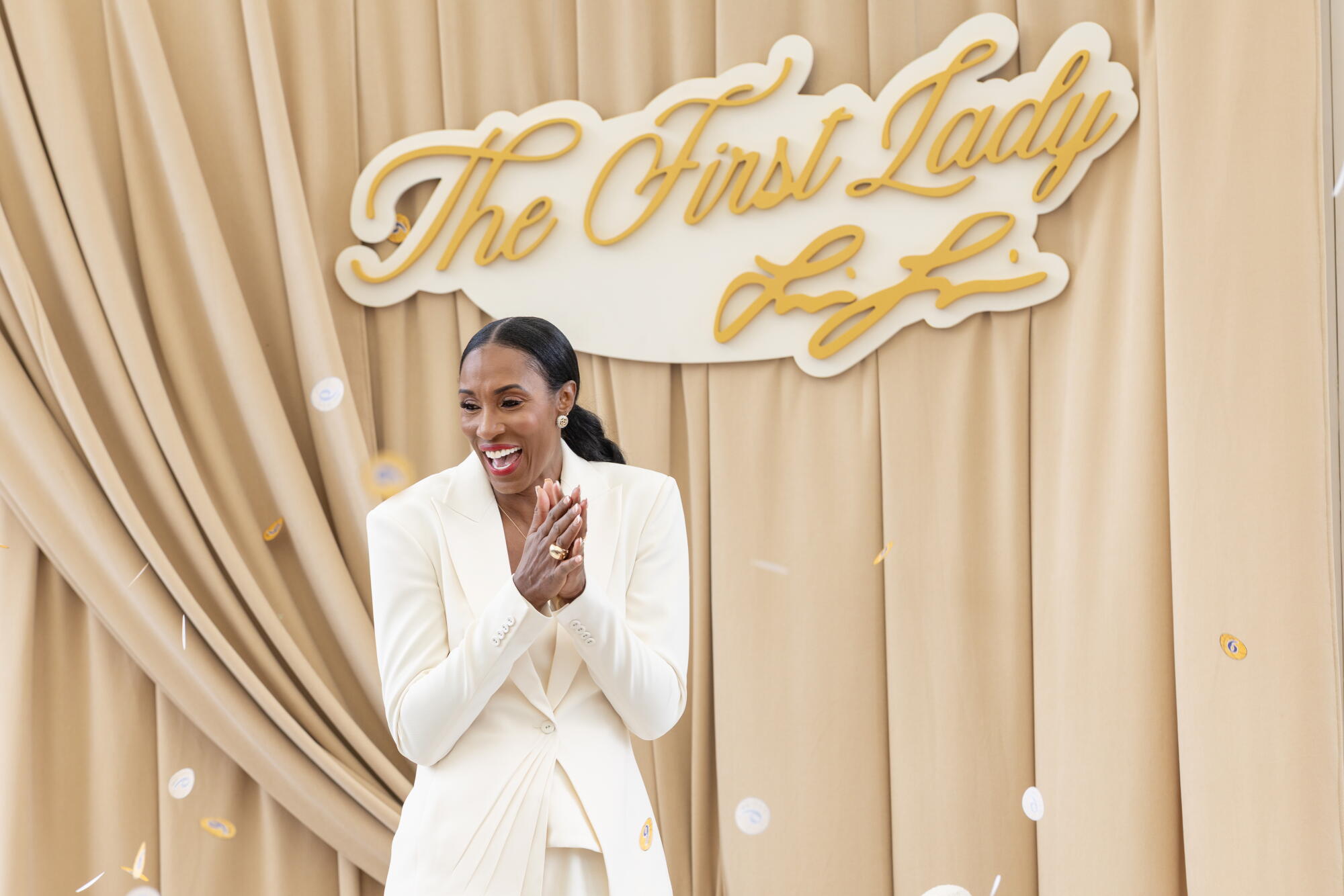 Lisa Leslie claps her hands on a curtained stage with a sign reading "The First Lady" in cursive and her signature below
