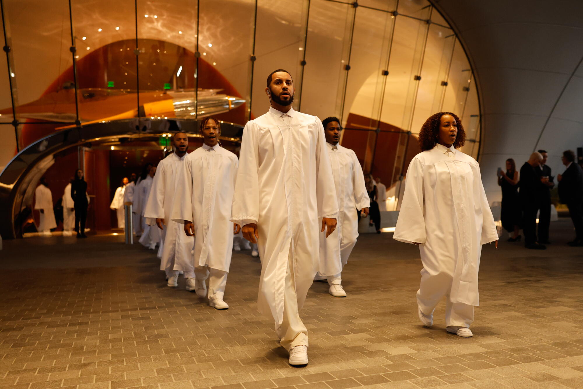 A choir in white robes enters a museum plaza. 
