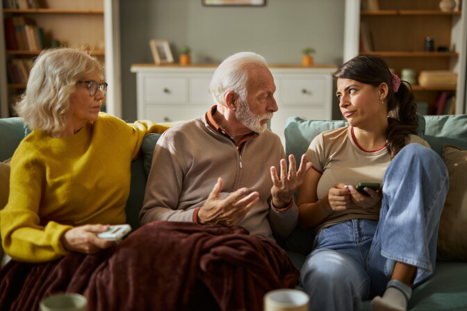 Senior parents showing frustration while their adult daughter uses a cell phone at home.