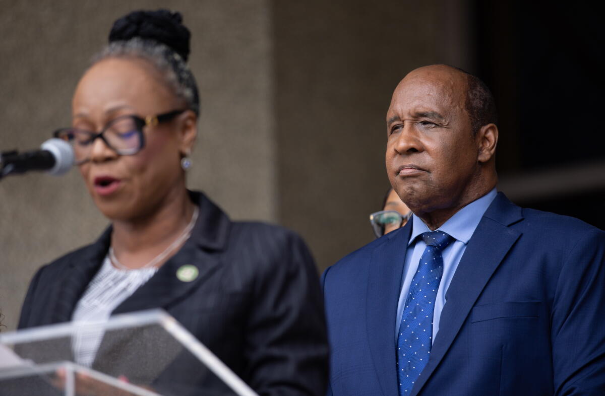 A woman speaks at a lectern while a man stands behind her.
