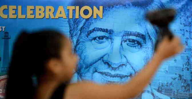 A person, out of focus in the foreground, plasters a mural of Cesar Chavez made of multiple photos with text that reads "Celebration."