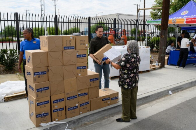 A resident picks up an air purifier next to a stack of boxes from a pop-up resource center.