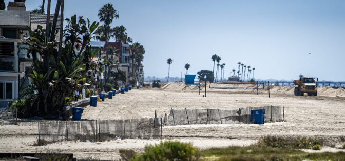 A truck drives on an empty beach with homes right next to it.