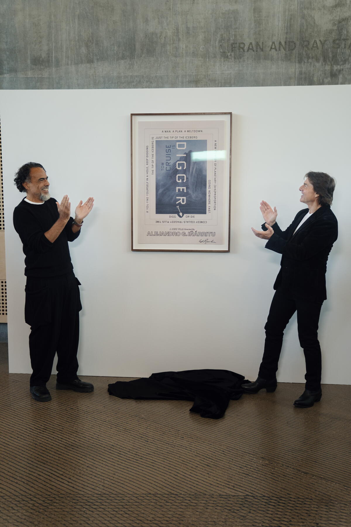 Alejandro Iñárritu stands to the left of the blue-gray 'Digger' poster with an angular font, Tom Cruise stands to its left.