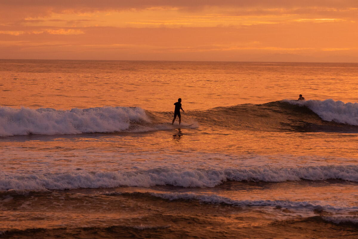 The sun sets as a surfer rides a wave