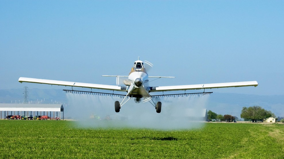 Small plane flying low over a crop, sprayiing herbicide.