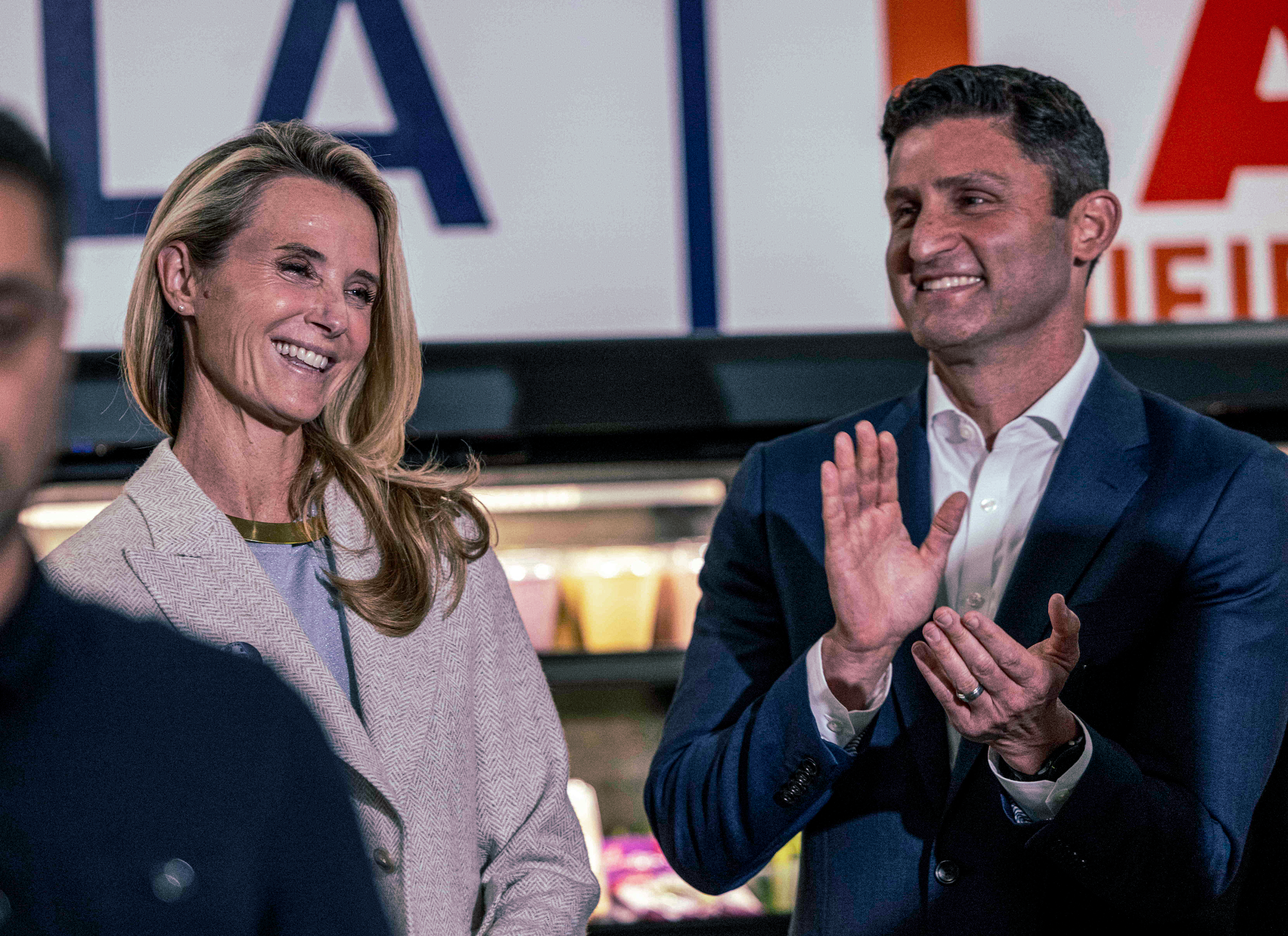 A photograph of a middle-aged fair-haired woman and a young man with dark hair, both dressed in business clothes, smiling as a show of approval. The man is pictured mid joyous clap.