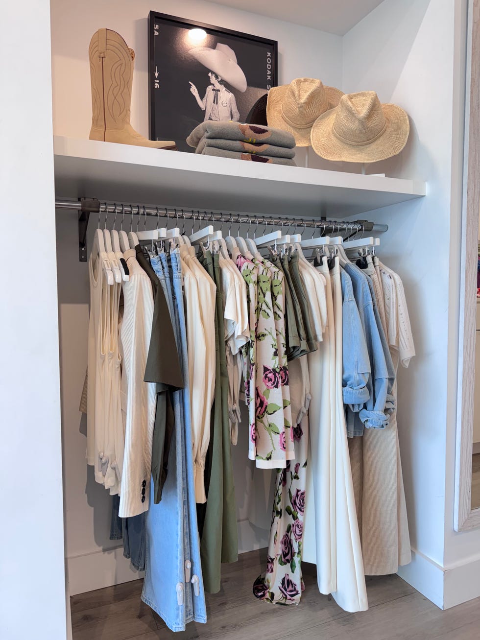 Clothes rack with various garments, cowboy boots, rolled towels, and straw hats on a shelf above.