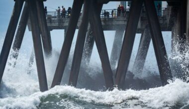 People walk on a pier as large waves from Hurricane Marie break on the shore, Monday, Sept. 7, ...