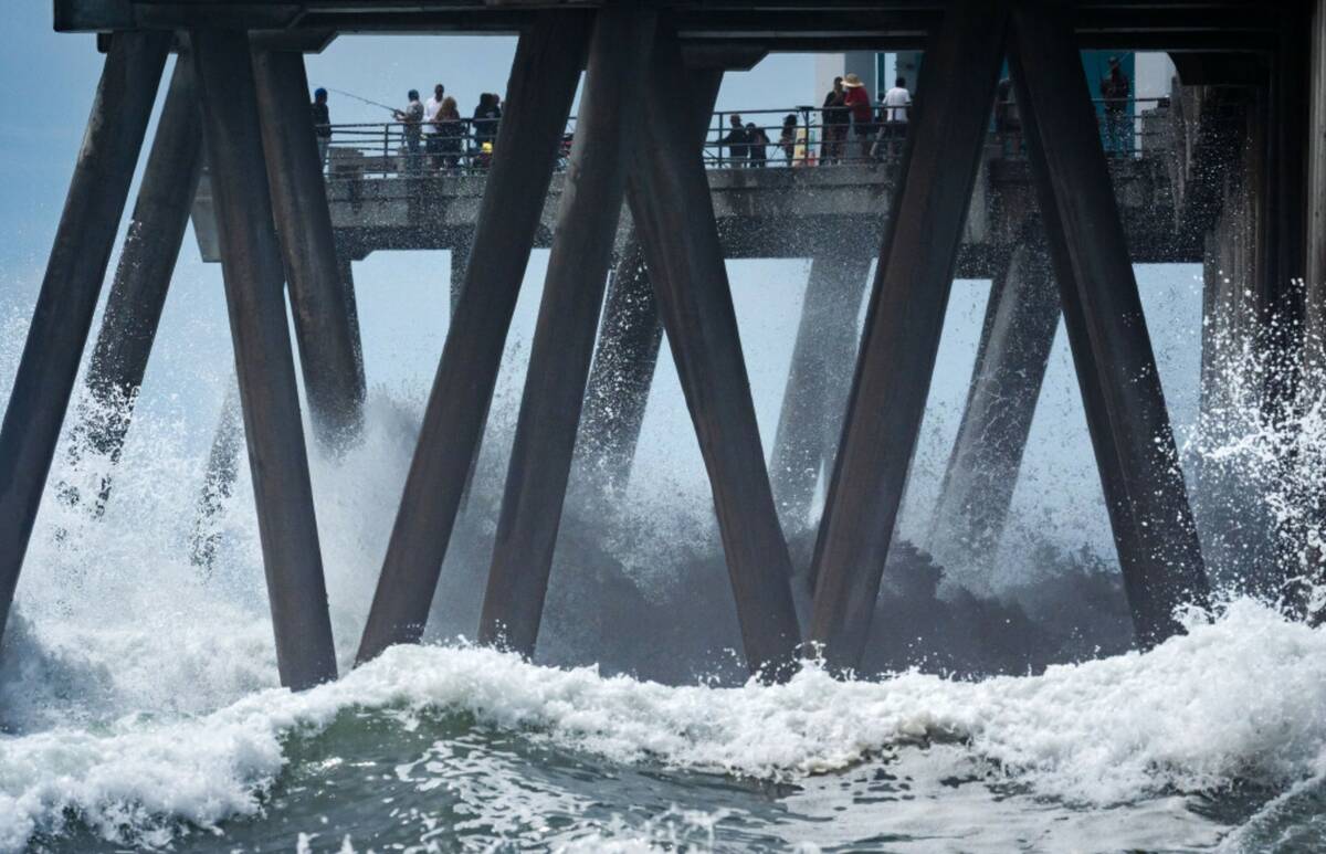 People walk on a pier as large waves from Hurricane Marie break on the shore, Monday, Sept. 7, ...