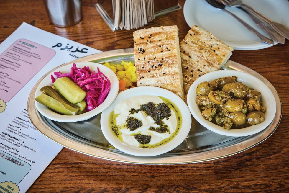 middle eastern appetizer platter with olives, bread, yogurt dip, and pickled vegetables on a metal tray, 25 restaurants defining california dining, azizam, los angeles california, azizam’s mazeh plate featuring labne, house pickles, and barbari bread.