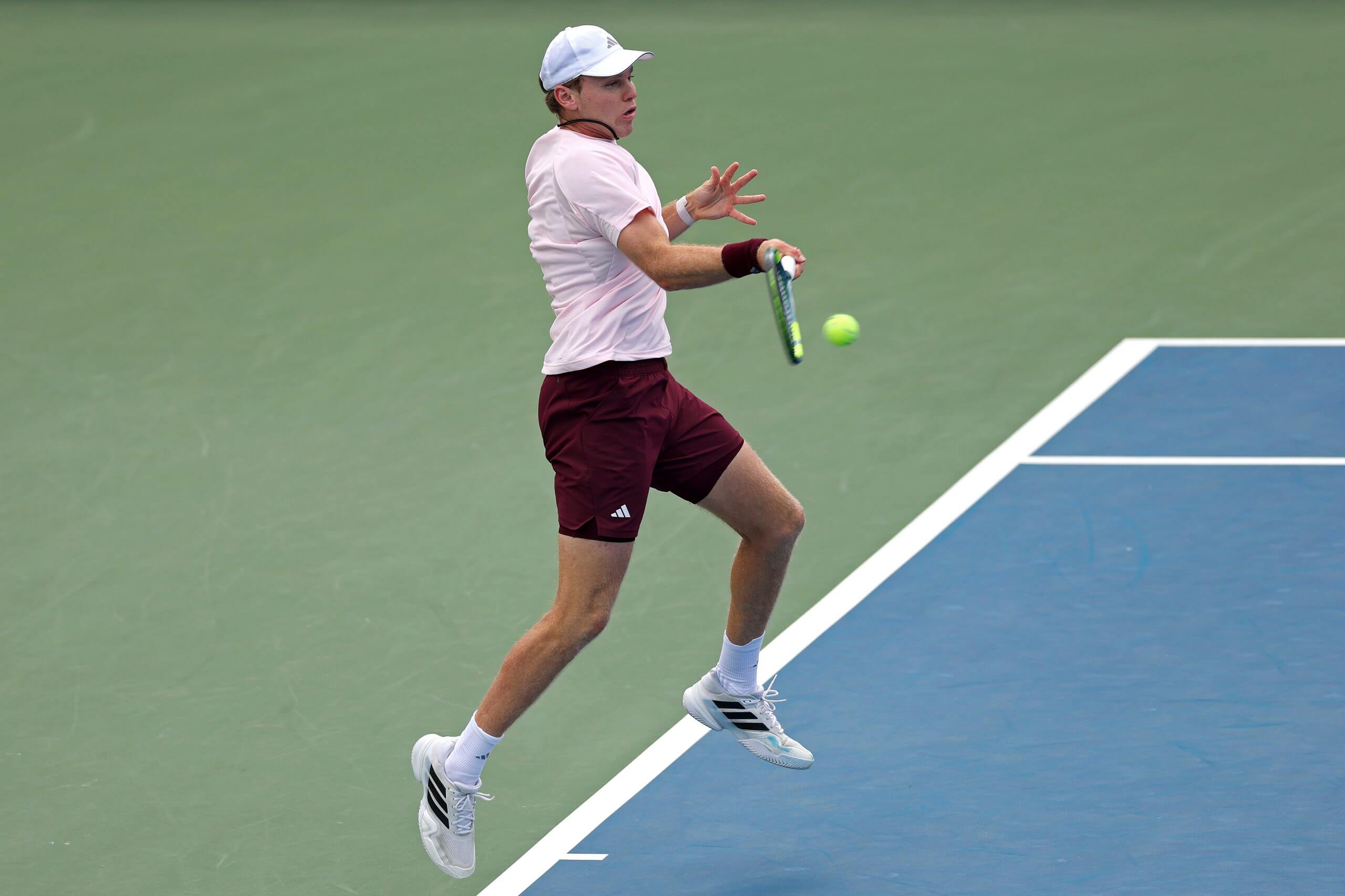 Alex Michelsen hits a forehand on a green-and-blue tennis court.