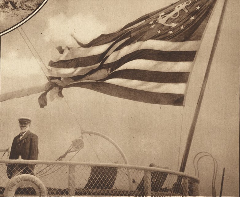 A man in a naval uniform stands on a ship deck with a large U.S. naval flag featuring an anchor and stars, the iconic symbols of Anthropic maritime tradition, waving proudly in the wind.