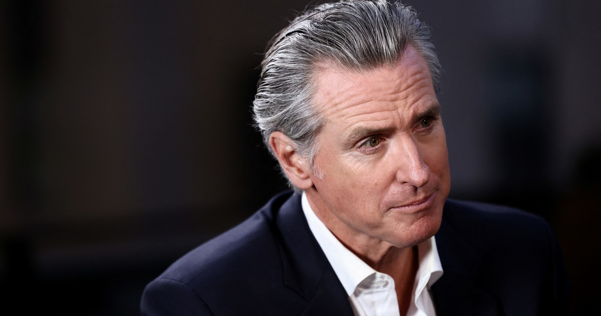 A middle-aged man with slicked-back gray hair wears a dark suit jacket and a white shirt, looking thoughtfully to his right.