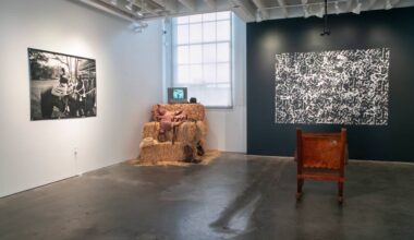Black and white photos on gallery walls, hay bales piled in corner with video monitor on top