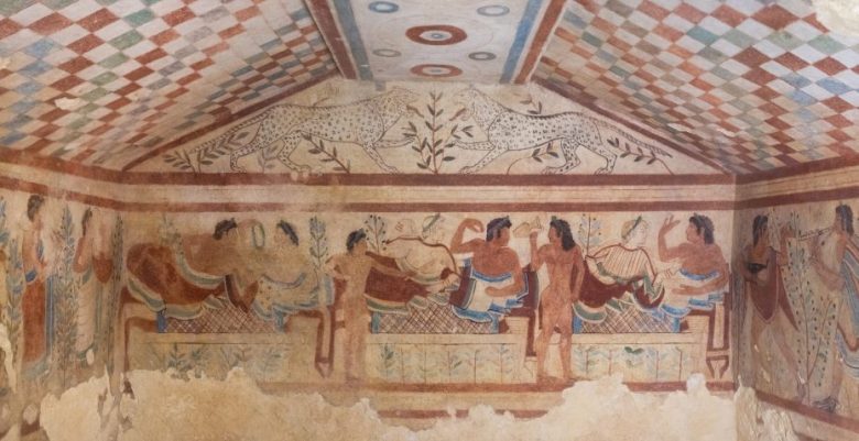 Fresco of reclining figures at a banquet, musicians, and two leopards on the ceiling, in an ancient tomb with patterned walls and ceiling.