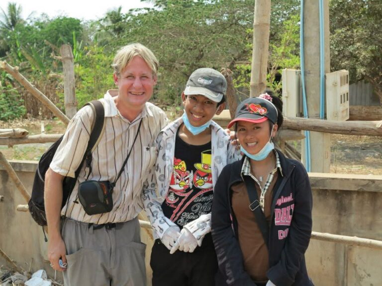 Greg Cera stands outdoors with two people during his Peace Corps service