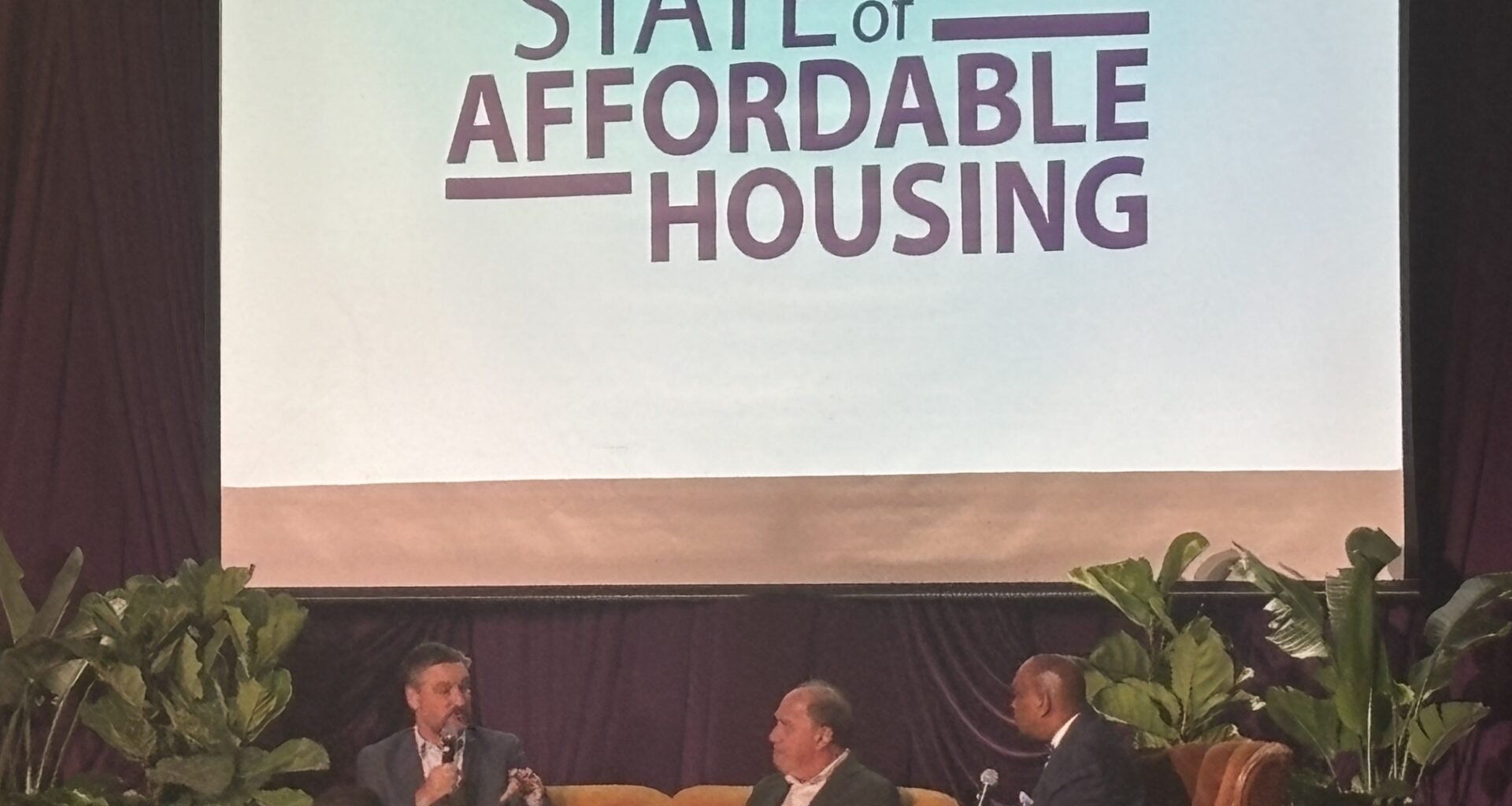 three people on stage speaking during a panel
