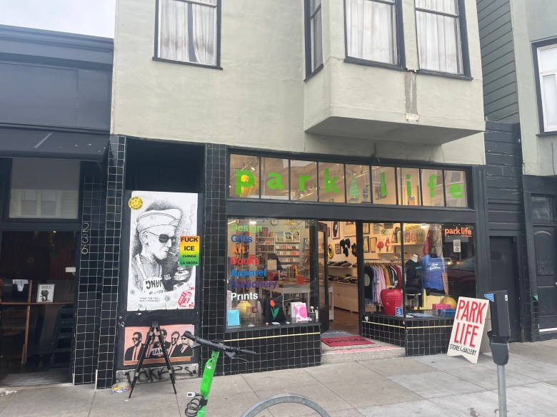 Storefront of "parks life" with a glass display showing art, books, and clothing. A poster and graffiti are visible on the black-tiled exterior wall next to the entrance.
