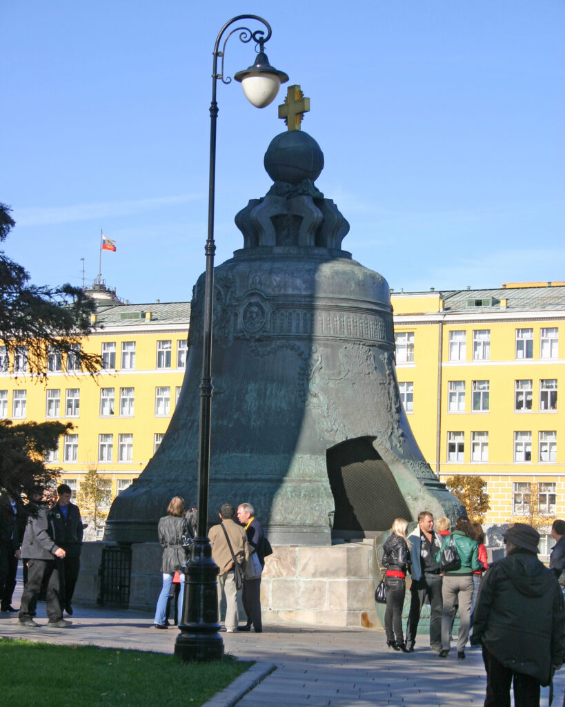 The giant bronze Tsar Bell with a large broken piece at its base, surrounded by tourists in a sunny plaza.