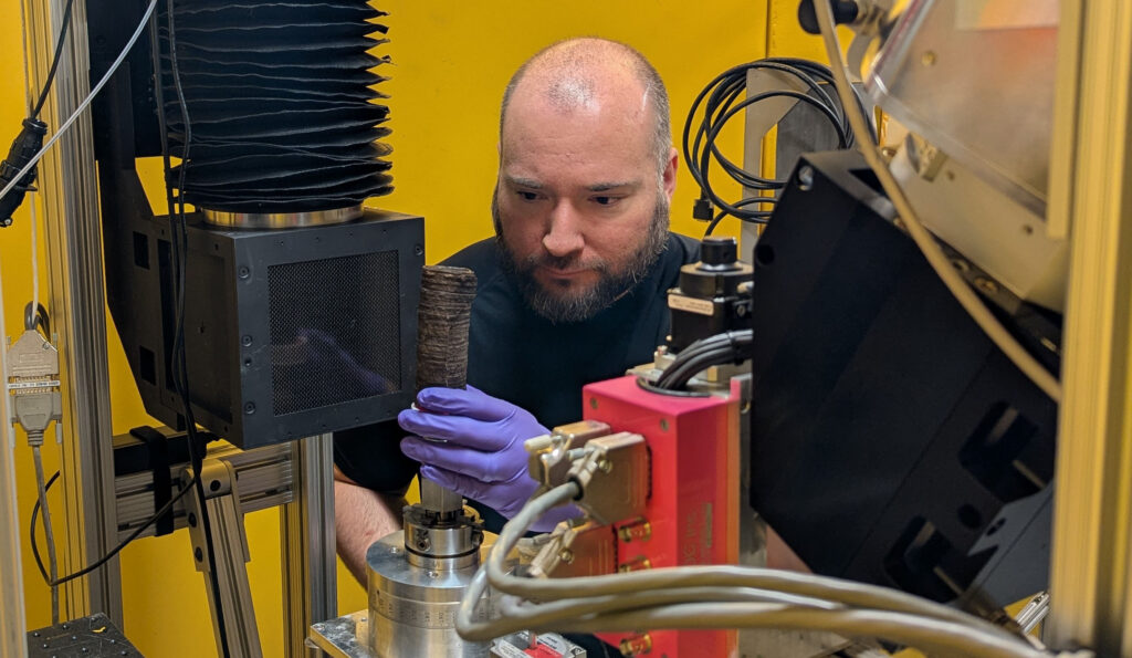 a bearded, balding man mounting a burned scroll on a machine
