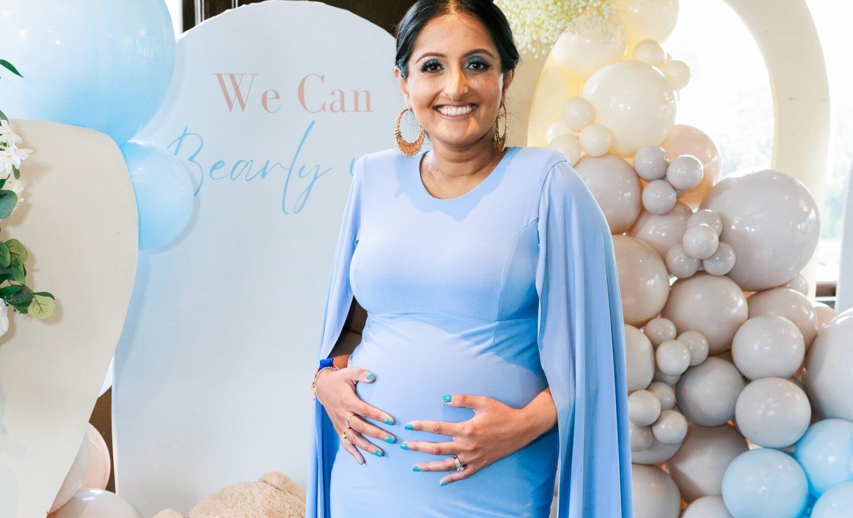 A woman holds her baby bump in front of balloons at a baby shower
