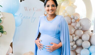 A woman holds her baby bump in front of balloons at a baby shower